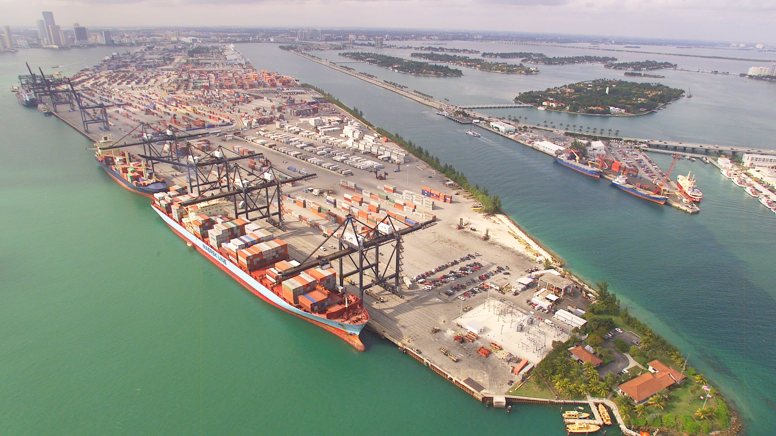 Aerial view of a port terminal with containers and cranes beside the water.